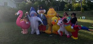 My best friends outdoors dressed in colorful, oversized inflatable costumes—such as a flamingo, shark, toy soldier, Garfield, duck, and unicorn—posing together on a sunny lawn. The joyful, playful scene captures the spirit of laughter, fun, and connection.